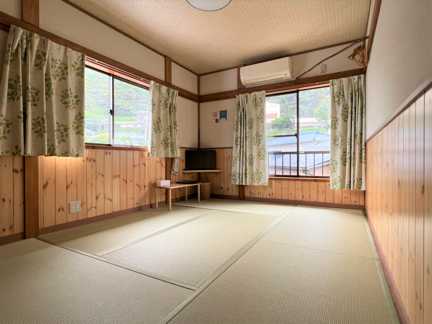 お宿 山じゅう — 御蔵島 · 緑葉柄のカーテン越しに集落と山影が見える、明るい和室
