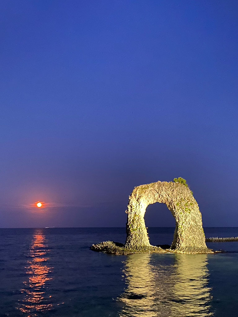 鍋釣岩の夕景 — 高さ19.5メートル、ライトアップされた奥尻島のシンボルと海に映る月明かり