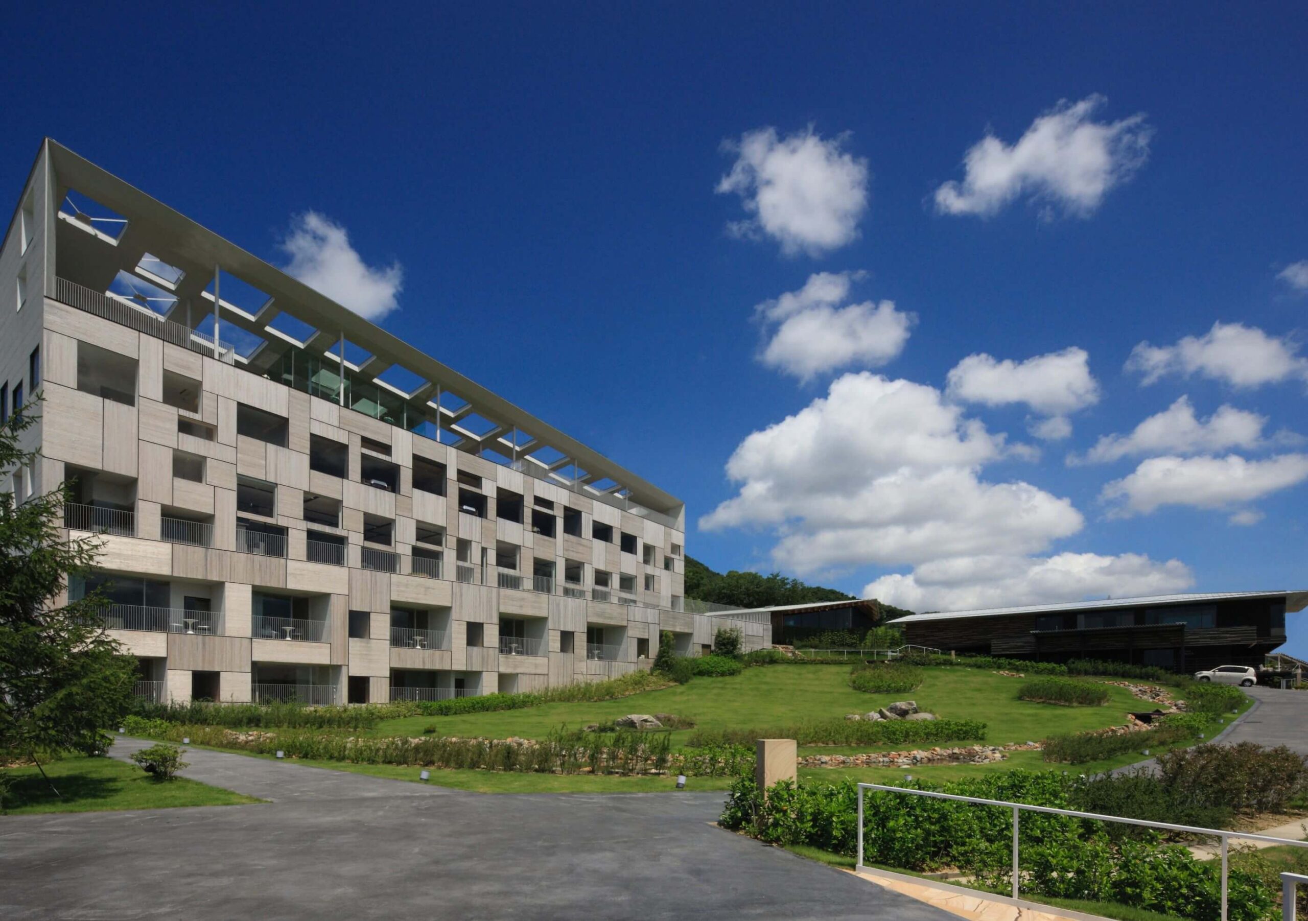 ガーデンテラス長崎 ホテル＆リゾート — 長崎市秋月町 · 石張りの客室棟と杉板の大屋根、芝生の庭が港へ向かって下る外観