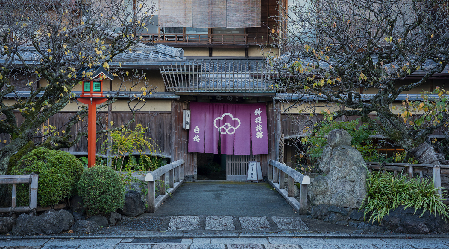 料理旅館 白梅 — 京都・祇園新橋 白川畔 · 白川に架かる石橋の先に構える、元お茶屋の玄関と暖簾