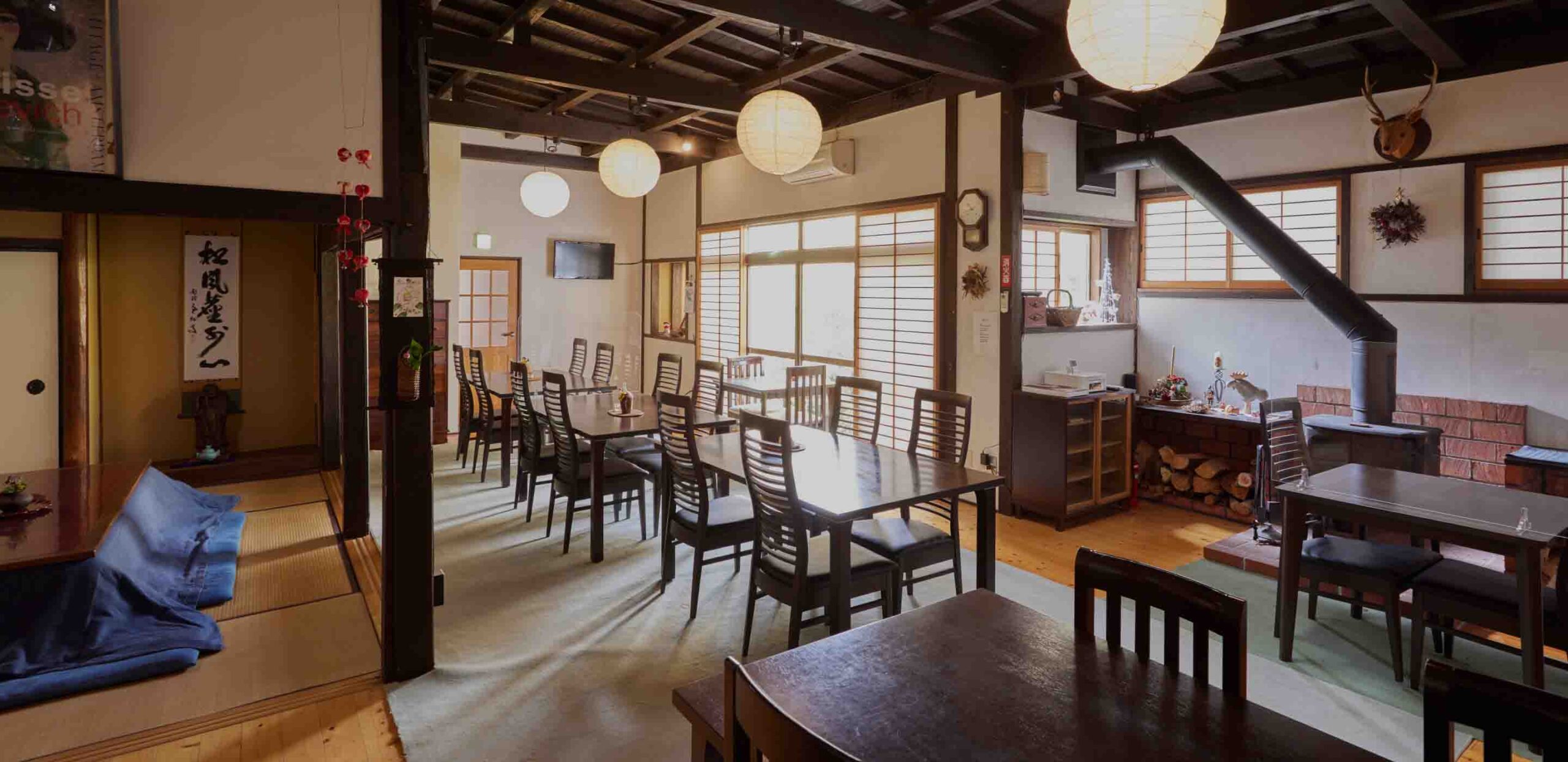 宿坊 対馬 西山寺 — 厳原町国分 · 梁を現した1階の食堂、薪ストーブと丸提灯が並ぶ朝食スペース