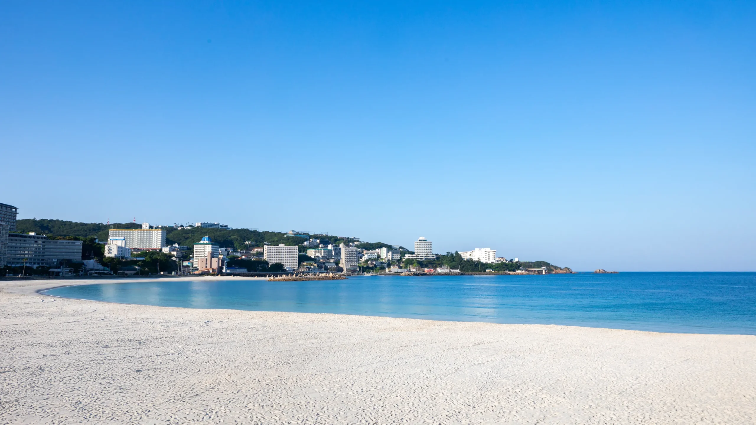 白良荘グランドホテル — 白浜町・白良浜直結 · 朝の白良浜と、湾の奥へ連なる温泉街の稜線