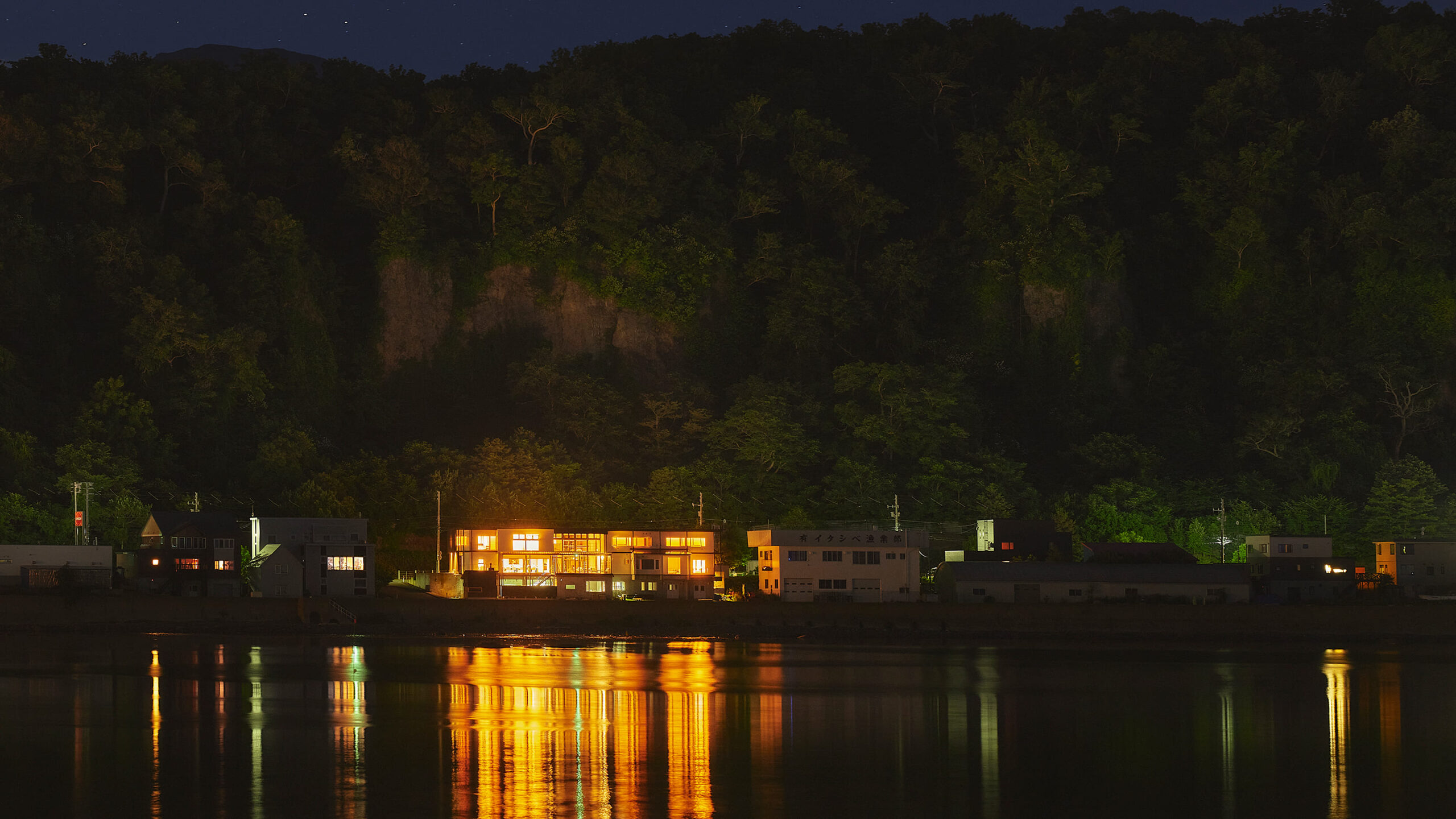 Lantern SHIRETOKO — 北海道斜里町ウトロ · オホーツク海の岸に灯る一棟貸しコテージの夜景、水面に映る窓明かり
