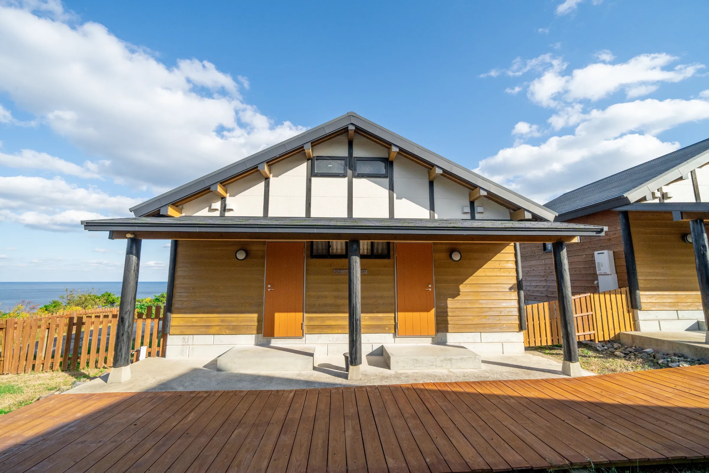対馬いづはらペンション — 厳原町東里 · 2室が入る切妻屋根のコテージと、柵の向こうに広がる対馬海峡の水平線