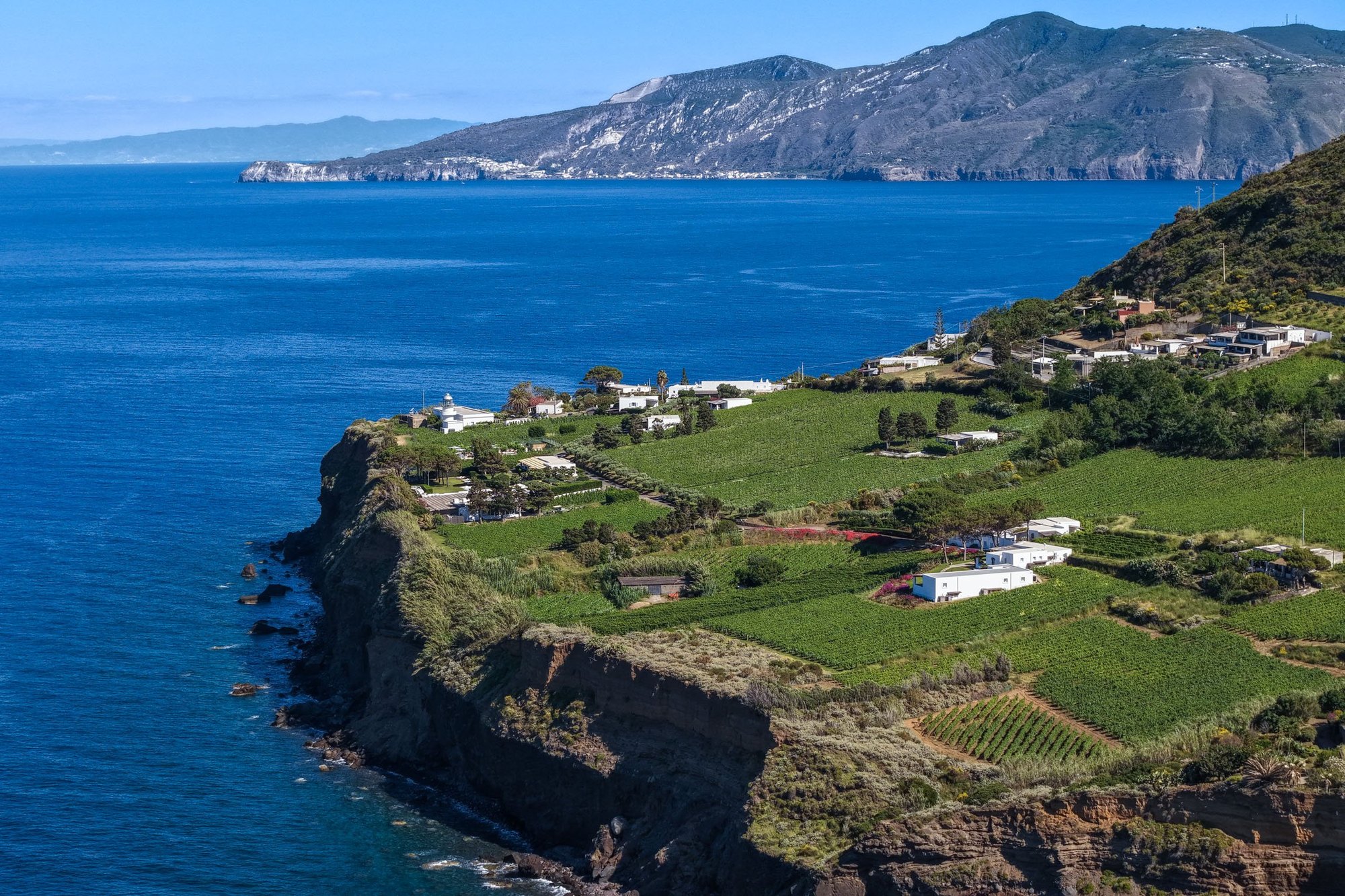 Capofaro Resort — エオリエ諸島サリーナ島マルファ · 断崖の上の葡萄畑と白い低層の客室、沖にリーパリの島影