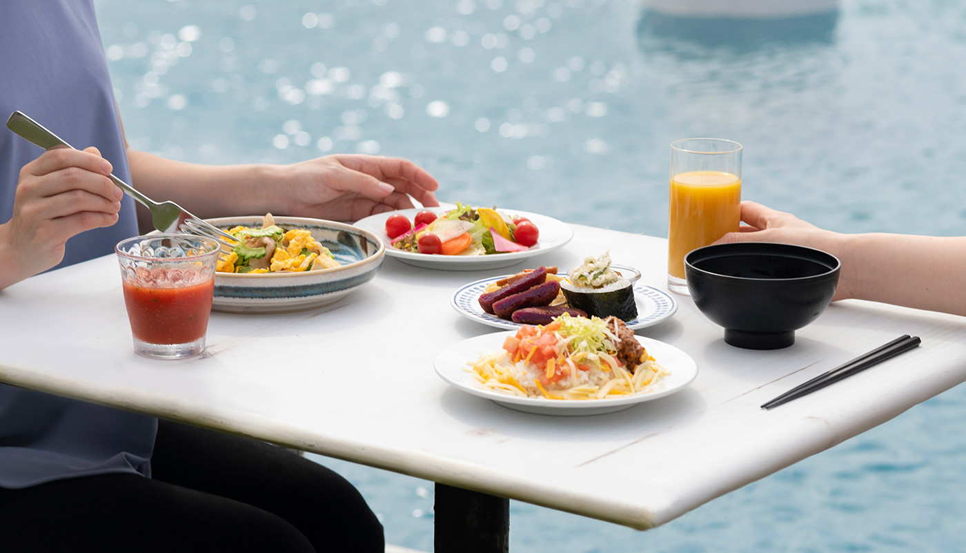 久米島イーフビーチホテル — THE OCEAN DINING · 海を背にしたテーブルに並ぶ沖縄料理の朝食