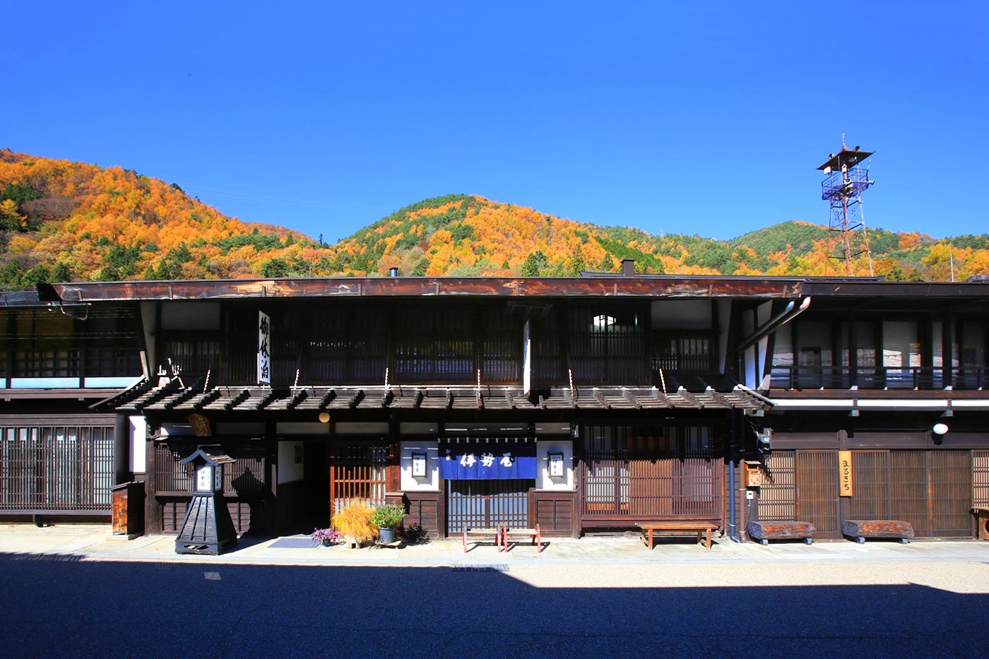 御宿 伊勢屋 — 長野県塩尻市・奈良井宿 · 紅葉の山を背に、千本格子と出梁造りの二階が通りに面する本館