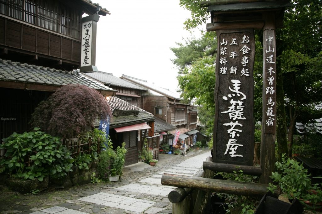 馬籠茶屋 — 岐阜県中津川市・馬籠宿 · 石畳の街道沿いに立つ木の看板と、坂に並ぶ宿場の家並み