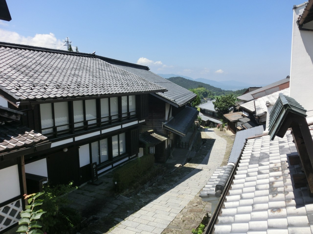但馬屋 — 岐阜県中津川市・馬籠宿 · 宿便りに掲載された、石置きの屋根が坂に沿って連なる宿場の眺め