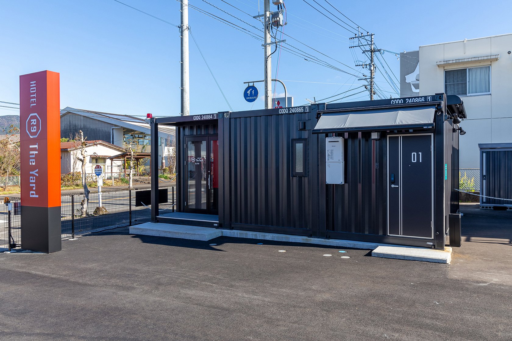 HOTEL R9 The Yard えびの — 宮崎県えびの市向江 · ブランドの看板とコンテナ型の客室が並ぶ入口