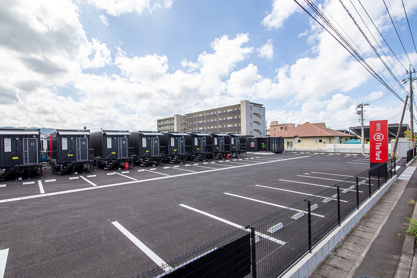HOTEL R9 The Yard 霧島国分 — 鹿児島県霧島市国分広瀬 · 平置きの駐車場に沿ってコンテナ型の客室が並ぶ