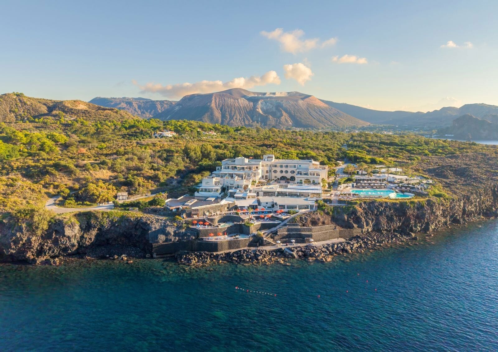 Therasia Resort Sea & Spa — エオリエ諸島ヴルカーノ島 · ヴルカネッロ岬の岩棚に建つ白いリゾートと背後の火口
